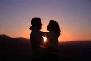 Couple hugging in front of the sun setting on the horizon.
