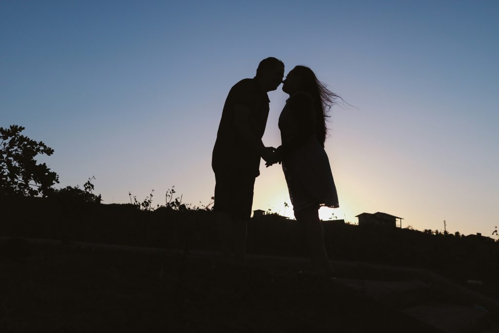 Sillouette of a couple holding hands with the sun rising on the background.