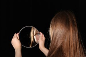 Woman looks at herself in a handheld mirror.