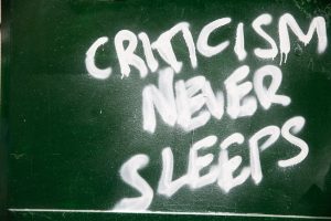 Graffiti on a green wall reads "criticism never sleeps"