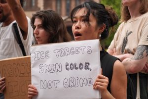 Woman holds sign: 'ice targets skin color, not crime'.