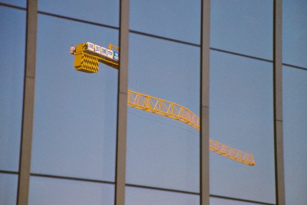 Yellow construction crane reflected on glass building