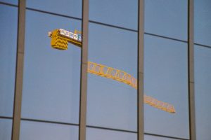 Yellow construction crane reflected on glass building