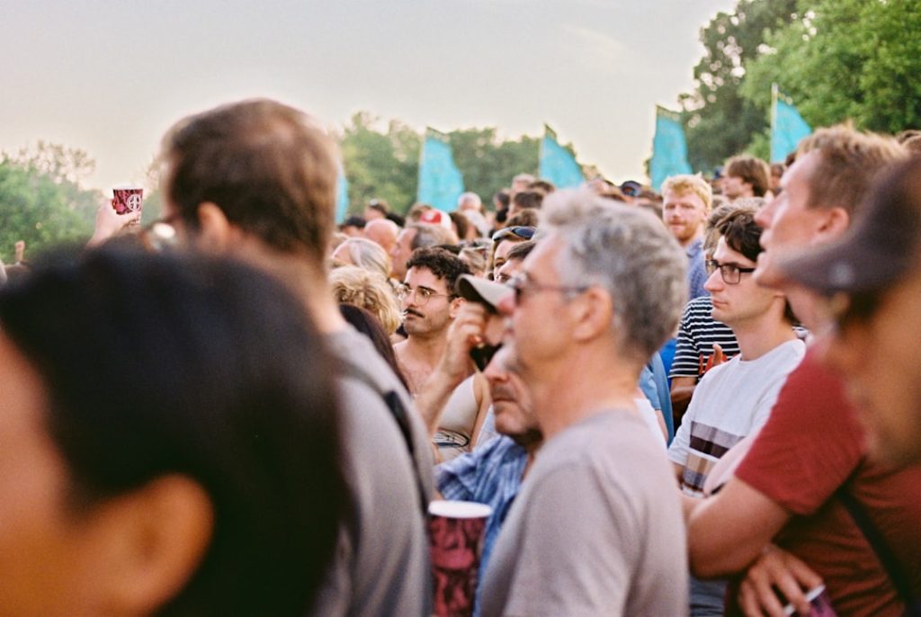 Festival-goers at golden hour, teal flags and trees