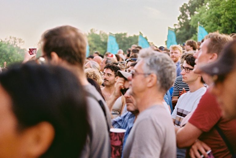 Festival-goers at golden hour, teal flags and trees