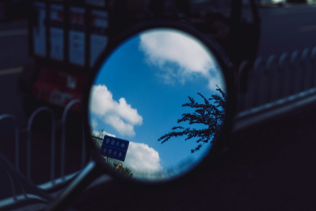 A rear view mirror reflecting a blue sky and clouds