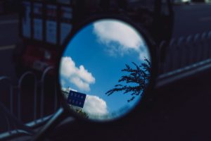 A rear view mirror reflecting a blue sky and clouds