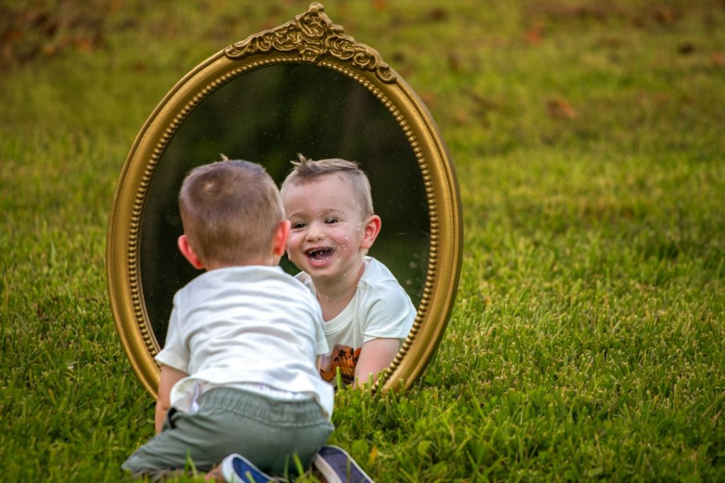 A baby smiles at their reflection in a mirror