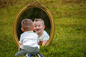 A baby smiles at their reflection in a mirror