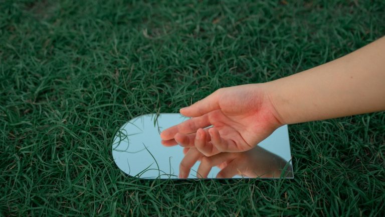 a person's hand touching a mirror on the grass