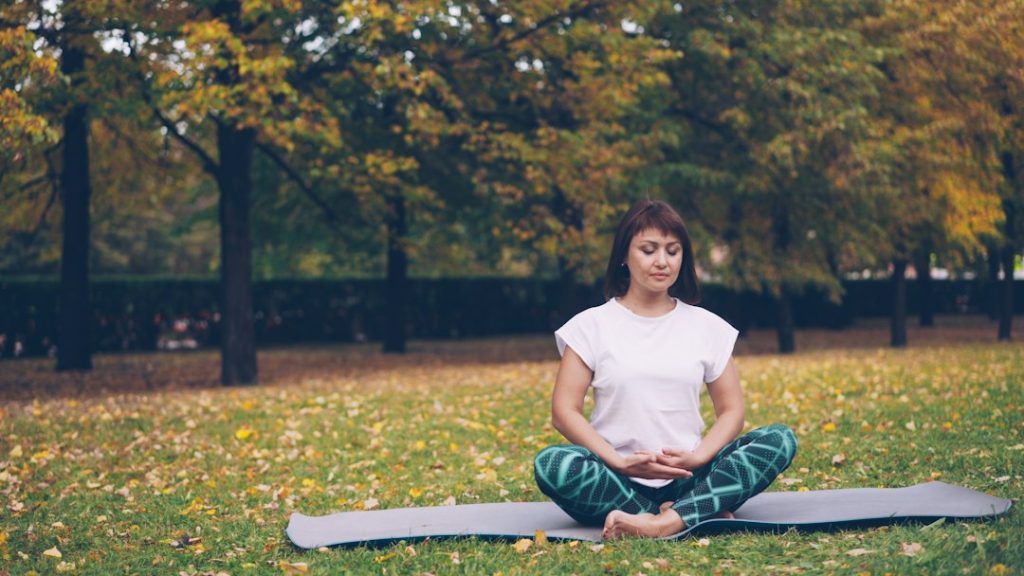 Woman meditating peacefully on yoga mat in autumn park